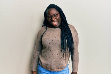 Saçları örgülü, gözlüklü genç siyahi bir kadın kameraya seksi bir ifadeyle bakıyor, neşeli ve mutlu bir yüzle.. 