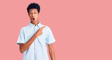 Gündelik giysiler giyen Afro-Amerikan genç adam parmaklarını yana çevirerek şaşırdı, ağzı açık hayret içinde kaldı.. 