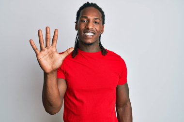 Saçları örgülü Afro-Amerikalı bir adam beş numarayı gösterip gösterirken kendinden emin ve mutlu bir şekilde gülümsüyor.. 