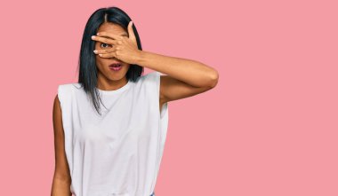 Genç Afro-Amerikalı kadın günlük giysiler giyiyor. Şok olmuş bir şekilde yüzünü ve gözlerini kapıyor. Utanmış bir ifadeyle parmaklarından bakıyor.. 