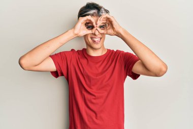 Günlük kıyafetler giyen genç İspanyol adam dürbün gibi jest yapıyor. Dürbün dilini çıkarıyor, gözler parmaklarından bakıyor. çılgın ifade. 