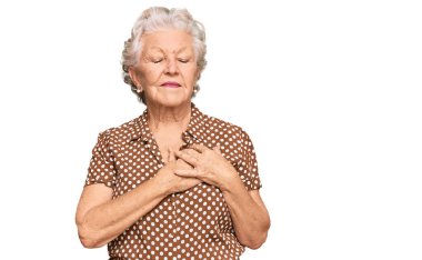 Üstün gri saçlı, günlük kıyafetler giyen, elleri göğsünde, gözleri kapalı gülümseyen ve yüzünde minnet ifadesi olan bir kadın. sağlık kavramı. 