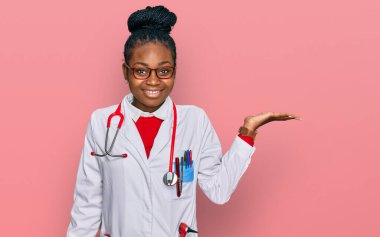 Genç Afrikalı Amerikalı kadın doktor üniforması ve steteskop giymiş neşeli bir şekilde gülümsüyor ve avuç içi kameraya bakıyor.. 