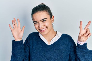 Kafkasyalı genç bir kız günlük kıyafetler giyer ve yedi numaralı parmaklarını göstererek mutlu ve kendinden emin bir şekilde gülümser.. 