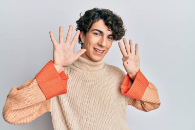 Latin kökenli genç adam, sıradan bir kazak giyip dokuz numaralı parmaklarıyla işaret ederken kendine güvenen ve mutlu bir şekilde gülümsüyor.. 