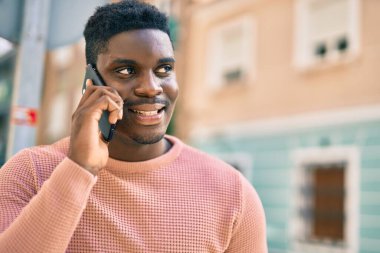 Genç Afrikalı Amerikalı gülümseyen mutlu bir adam şehirdeki akıllı telefondan konuşuyor..