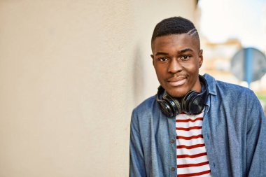 Genç Afrikalı Amerikalı adam şehirde kulaklık takarak mutlu bir şekilde gülümsüyor..