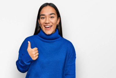 Kış süveteri giyen genç Asyalı kadın mutlu ve pozitif gülümsüyor, başparmağıyla mükemmel ve onay işareti yapıyor. 