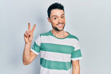 Gündelik kıyafetler giyen genç İspanyol adam kameraya bakıp zafer işareti yaparken parmaklarını gösteriyor. İki numara.. 