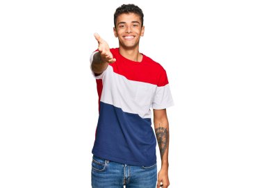 Genç, yakışıklı, Afro-Amerikalı, günlük kıyafetler giymiş, gülümseyen, dostça el sıkışan, hoş geldin diyen bir adam. başarılı iş. 