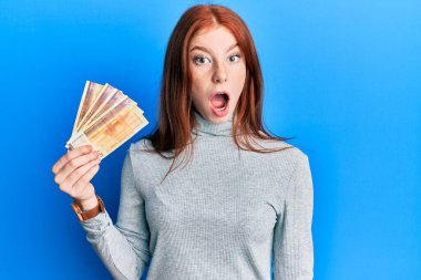 500 Norveçli kronu elinde tutan genç kızıl saçlı kız. Korkmuş ve şaşkın bir şekilde ağzı açık kalmış, inançsız bir yüz. 