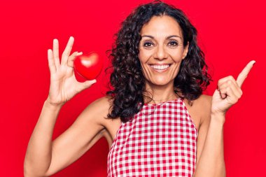 Orta yaşlı, kalbi olan güzel bir kadın gülümseyerek mutlu bir şekilde elini ve parmağını kenarda gezdiriyor. 