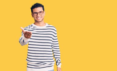 Gündelik kıyafetler ve gözlük takan İspanyol yakışıklı genç adam dostça bir selamlama ve hoş geldin hediyesi olarak el sıkışmayı sunuyor. başarılı iş. 