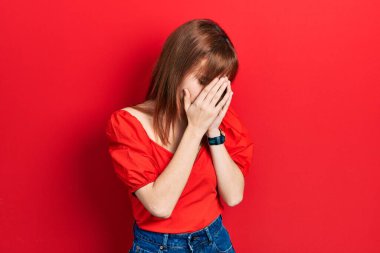 Kızıl saçlı genç kadın, ağlarken suratını ellerle kapatan sıradan kırmızı bir tişört giyiyor. depresyon kavramı. 