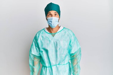 Cerrah üniforması ve tıbbi maske takan genç yakışıklı adam dudaklarıyla balık suratı yapıyor, çılgınca ve komik bir jest. Komik ifade. 