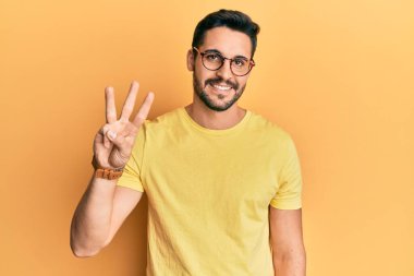 Gündelik kıyafetler giyen ve gözlük takan İspanyol genç adam üç numarayı gösterip işaret ederken kendinden emin ve mutlu bir şekilde gülümsüyor.. 