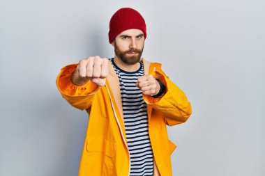 Sakallı, sarı yağmurluk giyen, dövüşmek için yumruk atan saldırgan ve öfkeli saldırı, tehdit ve şiddet içeren beyaz bir adam. 