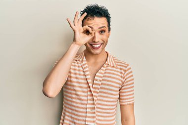 Makyaj yapan yakışıklı bir adam günlük tişört giyiyor. El hareketleriyle gülümsüyor, gözleriyle mutlu yüzüyle parmaklarının arasından bakıyor.. 