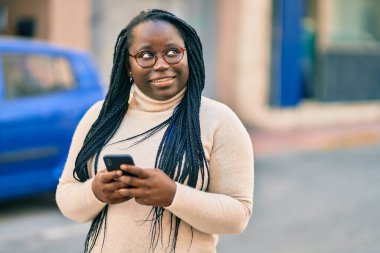 Genç Afrikalı Amerikalı kadın şehirde akıllı telefon kullanıyor..