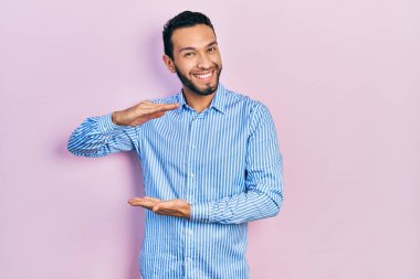 Sakallı, sıradan mavi gömlekli, elleri büyük ve büyük boy işareti gösteren İspanyol bir adam. Ölçü sembolü. Kameraya bakıp gülümsüyor. ölçüm kavramı. 