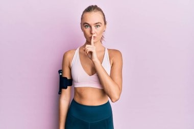 Spor kıyafetleri ve kol bandı takan güzel sarışın kadın sessiz olmak istiyor. sessizlik ve gizli konsept. 