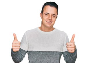 Kış süveteri giyen yakışıklı genç adam elinde olumlu bir jest yapıyor, gülümsüyor ve mutlu. Neşeli ifade ve kazanan jest. 