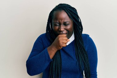 Örgülü, sıradan kıyafetler giyen, kendini kötü hisseden ve soğuk algınlığı veya bronşitin belirtisi olarak öksüren genç siyahi bir kadın. sağlık hizmeti kavramı. 