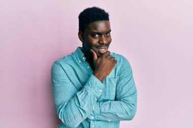 Yakışıklı, sıradan kıyafetler giyen, kameraya kendinden emin, kollarını kavuşturup gülümseyen ve çenesini kaldıran siyahi adam. Olumlu düşünmek. 