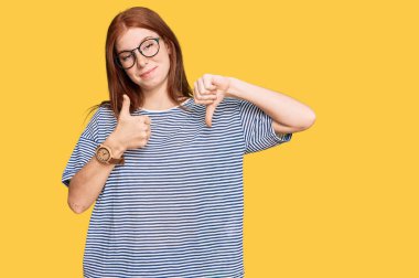 Young read head woman wearing casual clothes and glasses doing thumbs up and down, disagreement and agreement expression. crazy conflict  clipart