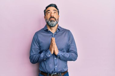 Orta yaşlı, sakallı, gri saçlı iş kıyafetleri giyen, elleri bağlı yalvaran ve dua eden, yüzünde umut ifadesi olan çok duygusal ve endişeli bir adam. Yalvarıyor. 