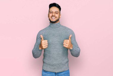 Gündelik kıyafet giyen genç bir Arap. Başarı işareti yapıyor. Elleriyle olumlu jest yapıyor. Neşeli ifade ve kazanan jest. 