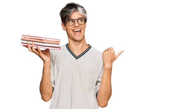 Jovem Hispânico Segurando Livros Apontando Polegar Para Lado Sorrindo Feliz — Fotografia de Stock