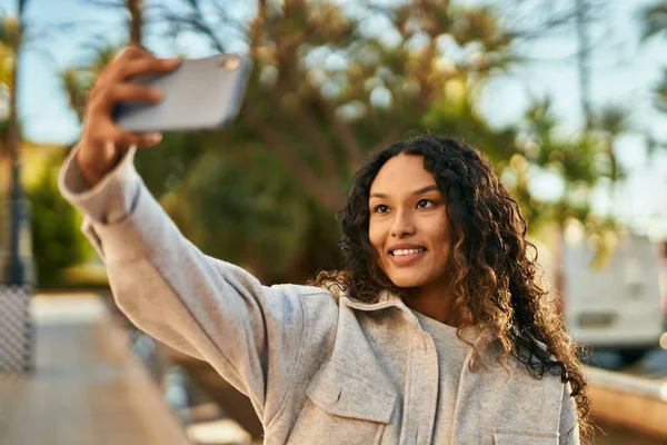 Young latin woman smiling happy making selfie by the smartphone at the city.