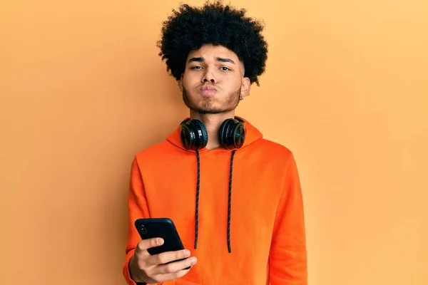 年轻的非洲裔美国人 留着非洲裔头发 用智能手机用滑稽的脸蛋鼓起双颊 嘴被空气吹胀 — 图库照片