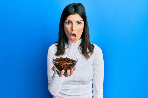 Young Hispanic Woman Holding Raisins Bowl Scared Amazed Open Mouth — Stock Photo, Image