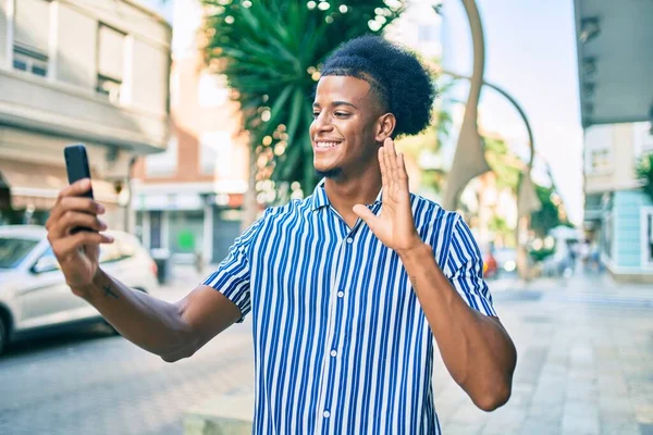 若いアフリカ系アメリカ人の男が笑顔でビデオ通話をしています市内でスマートフォンを使って — ストック写真