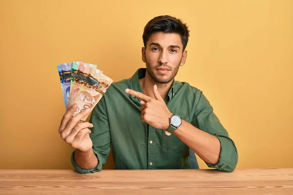 Młody Przystojny Mężczyzna Trzymający Kanadyjskie Dolary Wskazując Palcem Stronę Pokazując — Zdjęcie stockowe