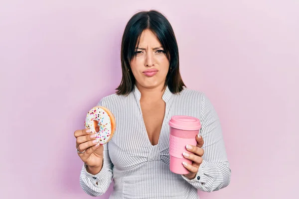 Ung Latinamerikansk Kvinna Äter Munk Och Dricker Kaffe Skeptisk Och — Stockfoto