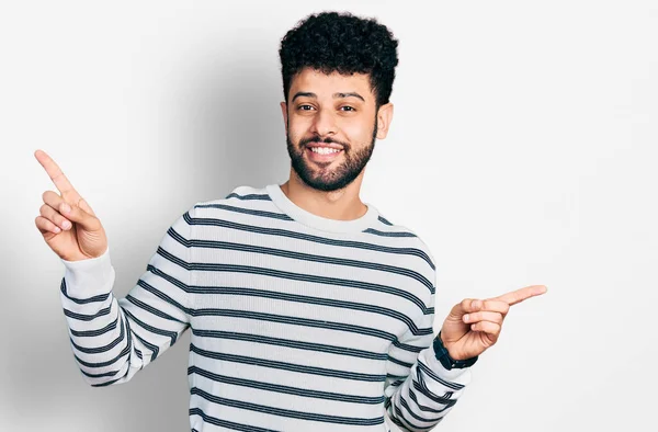 年轻的阿拉伯男子 留着胡子 穿着随意的条纹毛衣 带着自信的微笑 用手指指向不同的方向 复制广告空间 — 图库照片