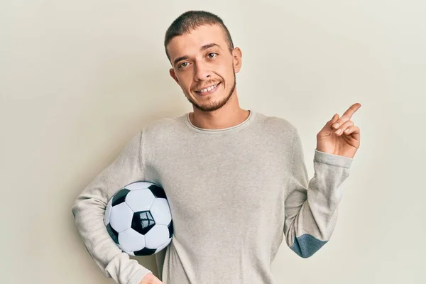 Latynos Młody Człowiek Trzymając Piłkę Nożną Uśmiecha Się Szczęśliwy Wskazując — Zdjęcie stockowe