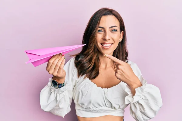年轻的黑发女子牵着粉红的纸飞机 高兴地微笑着 手指手画脚 — 图库照片