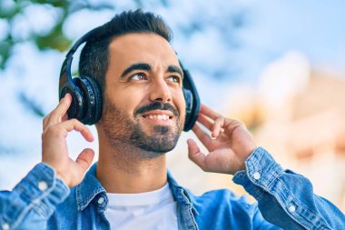 Şehirde kulaklık takarak mutlu gülümseyen genç İspanyol adam..