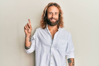 Sakallı, uzun saçlı, sıradan beyaz tişörtlü, mutlu yüzüyle bir fikir veya soruyla gülümseyen yakışıklı bir adam. 