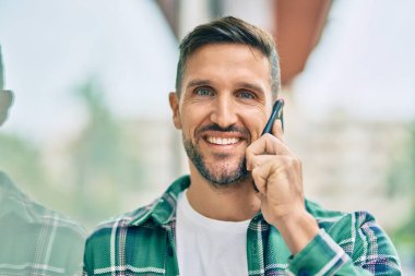 Genç beyaz adam gülümsüyor. Şehirdeki akıllı telefondan konuşuyor..