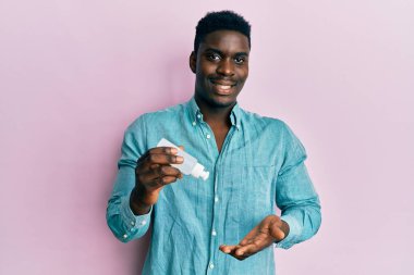 Yüzünde mutlu ve havalı bir gülümsemeyle gülümseyen el dezenfektanı jeli yakışıklı bir zenci. diş gösterme. 