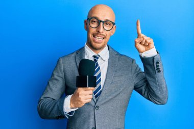 Sakallı kel adam elinde mikrofonla gülümsüyor bir fikri olan ya da soru işareti yapan mutlu yüzlü, bir numara. 