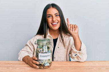 Güzel İspanyol bir kadın elinde para dolu bir kavanozla bir fikri ya da sorusu olan mutlu bir yüzü olan bir kadını işaret ediyor. 