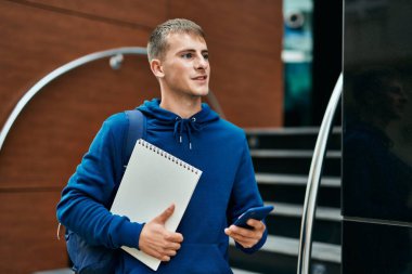 Üniversitede akıllı telefon kullanan genç sarışın bir öğrenci..