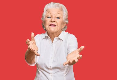 Son sınıftaki gri saçlı kadın, günlük kıyafetler giyip kameraya bakıyor ve sarılmak için kollarını açmış gülümsüyor. Mutluluğu kucaklayan neşeli bir ifade.. 