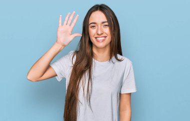 Gündelik beyaz tişört giyen genç İspanyol kız beş numarayı gösterip işaret ederken kendinden emin ve mutlu bir şekilde gülümsüyor.. 